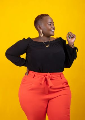 Plus size lady wearing orange trousers and a black dress accesorizing.